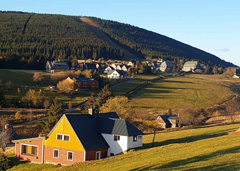 Podzimní krajina s domy v údolí pod zalesněným svahem